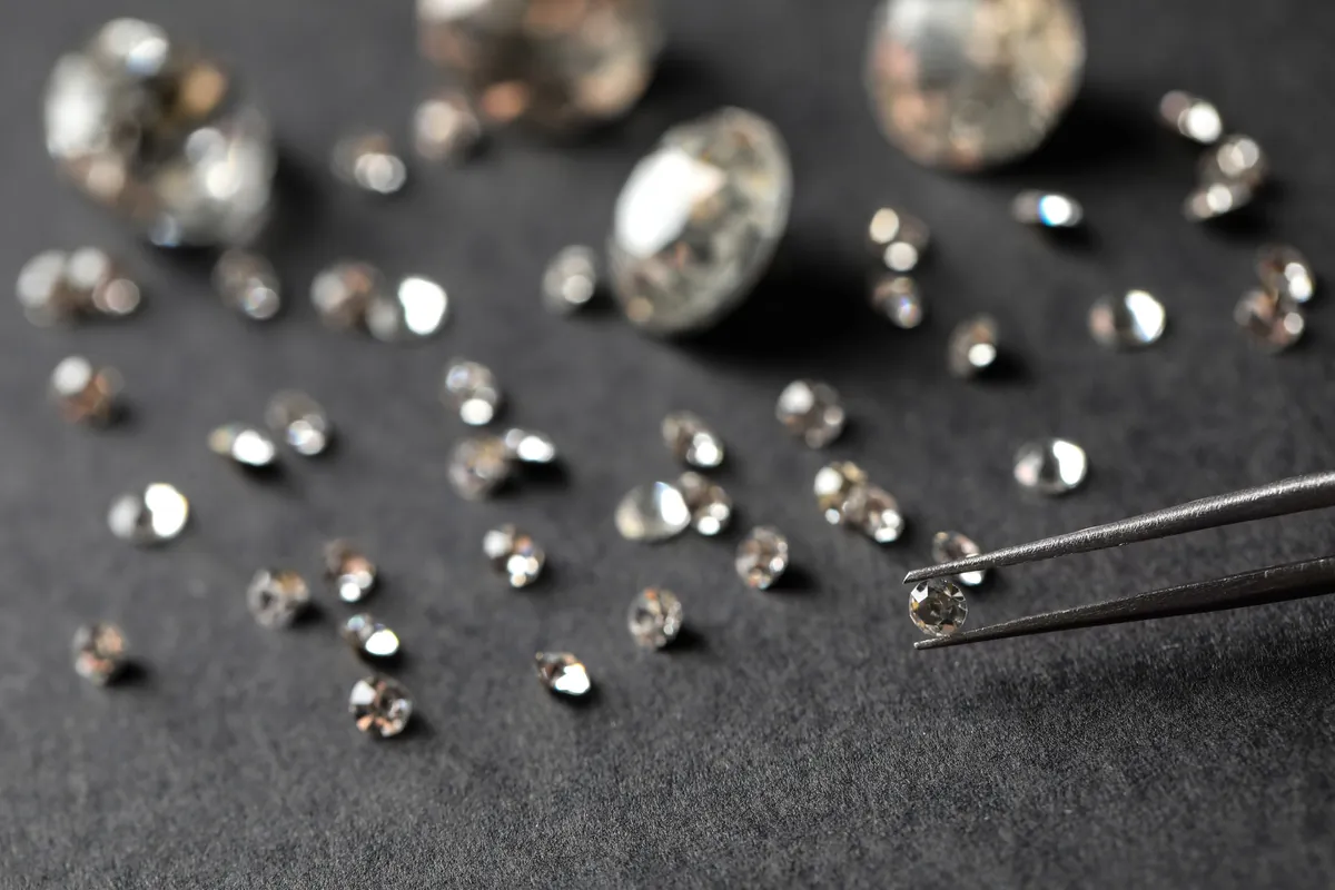 Eine Metallpinzette hält einen Diamanten im Brillantschliff über losen Steinen