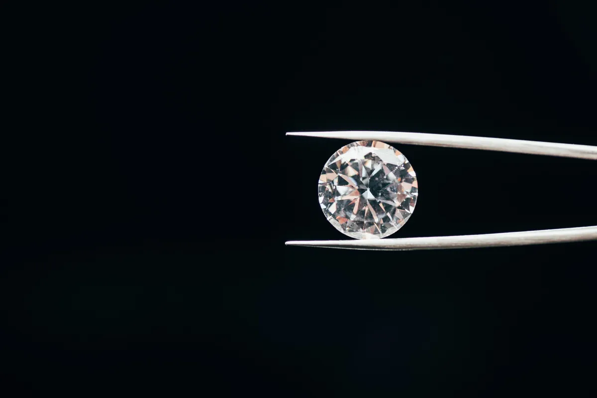 Ein Diamant im Brillantschliff in einer Pinzette vor schwarzem Hintergrund