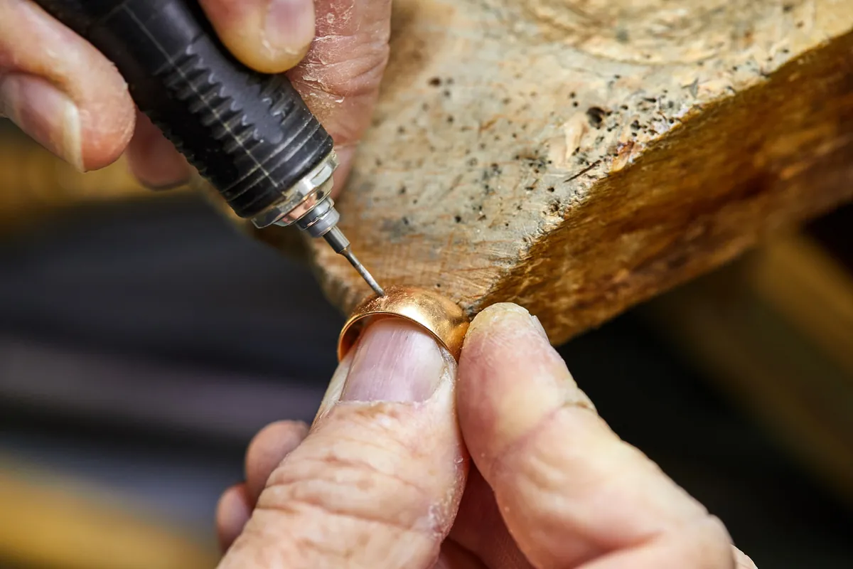 Ein Goldschmied bearbeitet die Innenseite eines Goldrings mit einem feinen Werkzeug