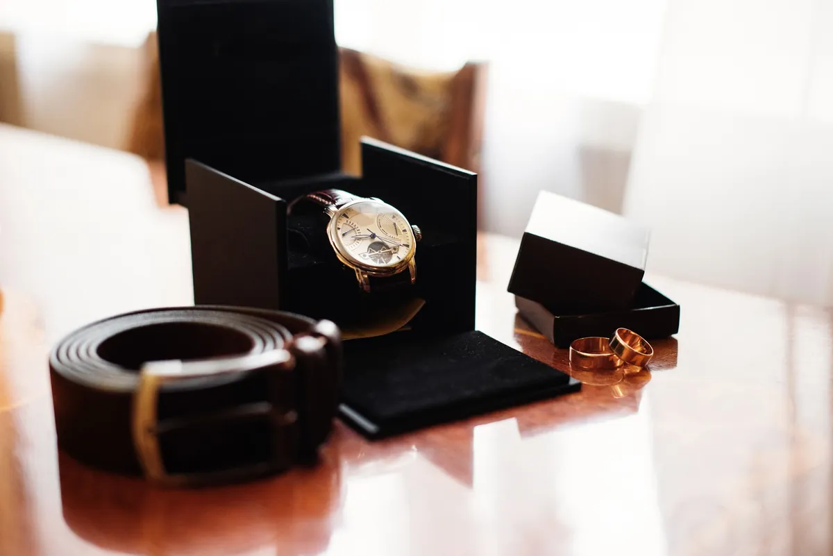 Eine Dresswatch in ihrer Präsentationsbox neben einem Ledergürtel und zwei Ringen