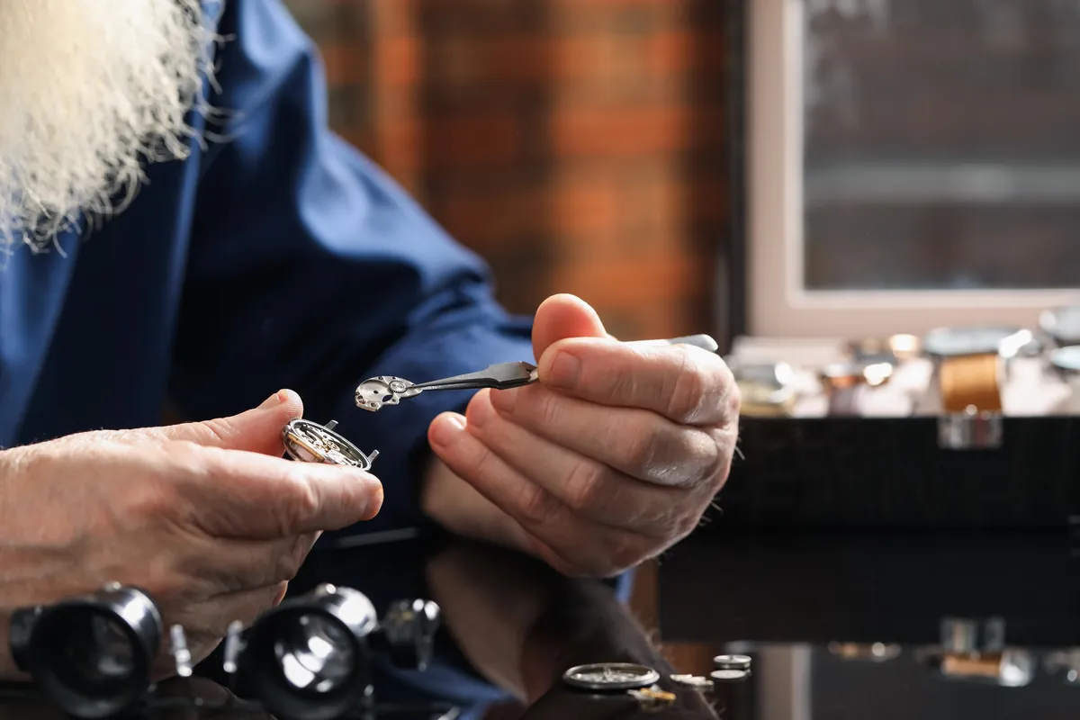 Ein älterer Uhrmacher repariert sorgfältig eine mechanische Uhr an seiner Werkbank